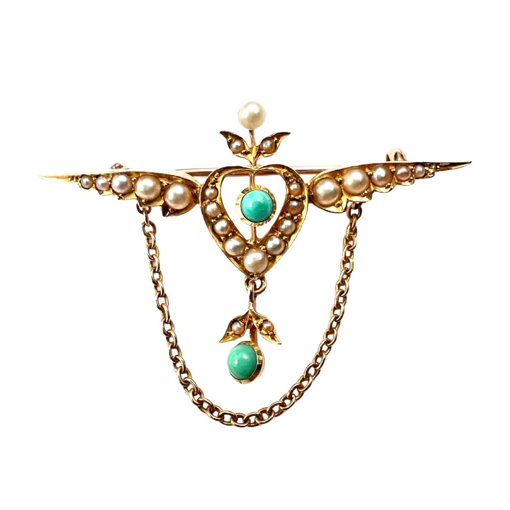 An Edwardian 15ct gold brooch featuring a winged heart motif set with seed pearls and turquoise cabochons with a draped lower chain.