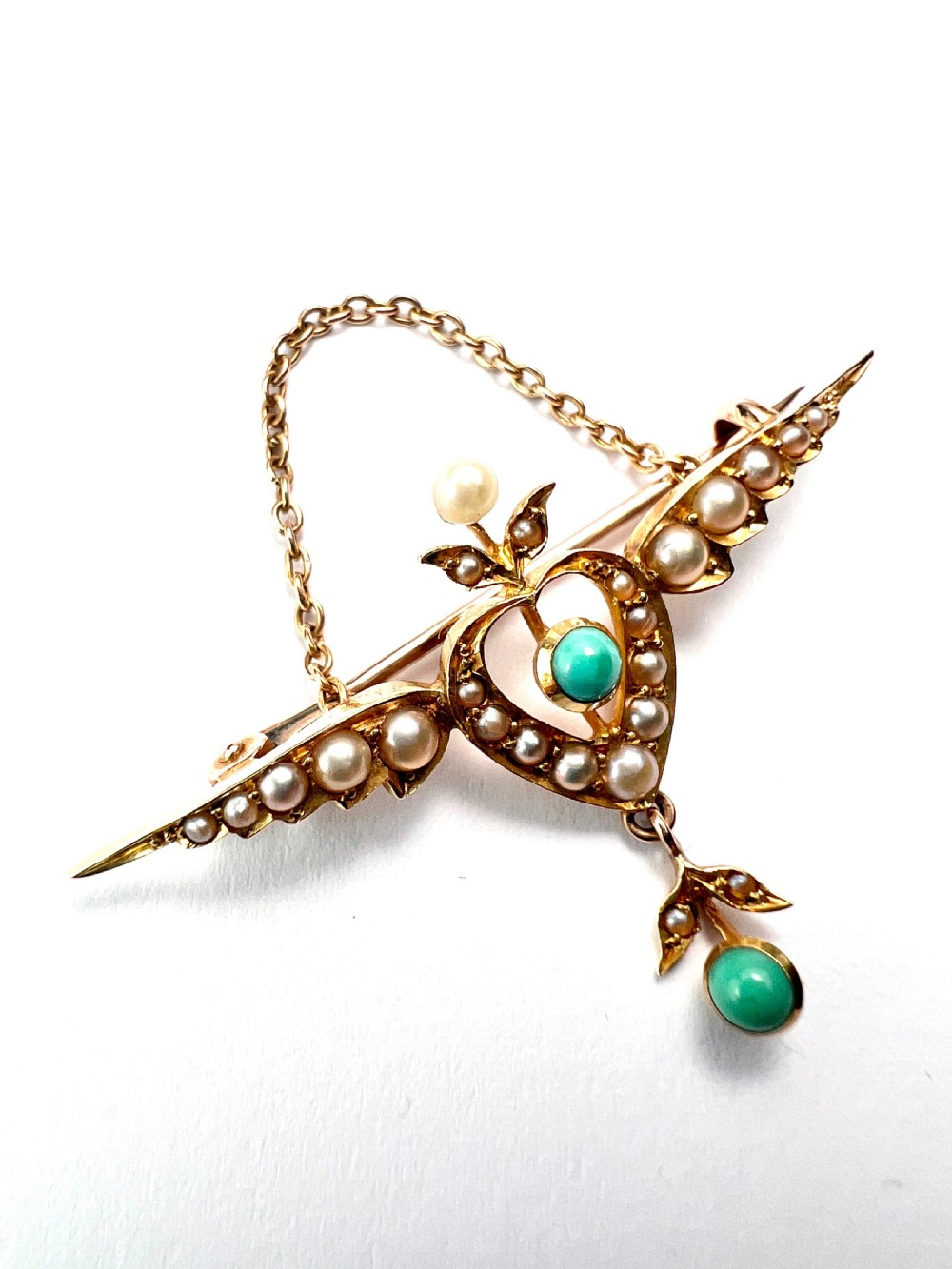 An Edwardian 15ct gold brooch featuring a winged heart motif set with seed pearls and turquoise cabochons with a draped lower chain. View VII