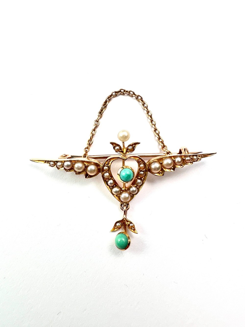 An Edwardian 15ct gold brooch featuring a winged heart motif set with seed pearls and turquoise cabochons with a draped lower chain. View VIII
