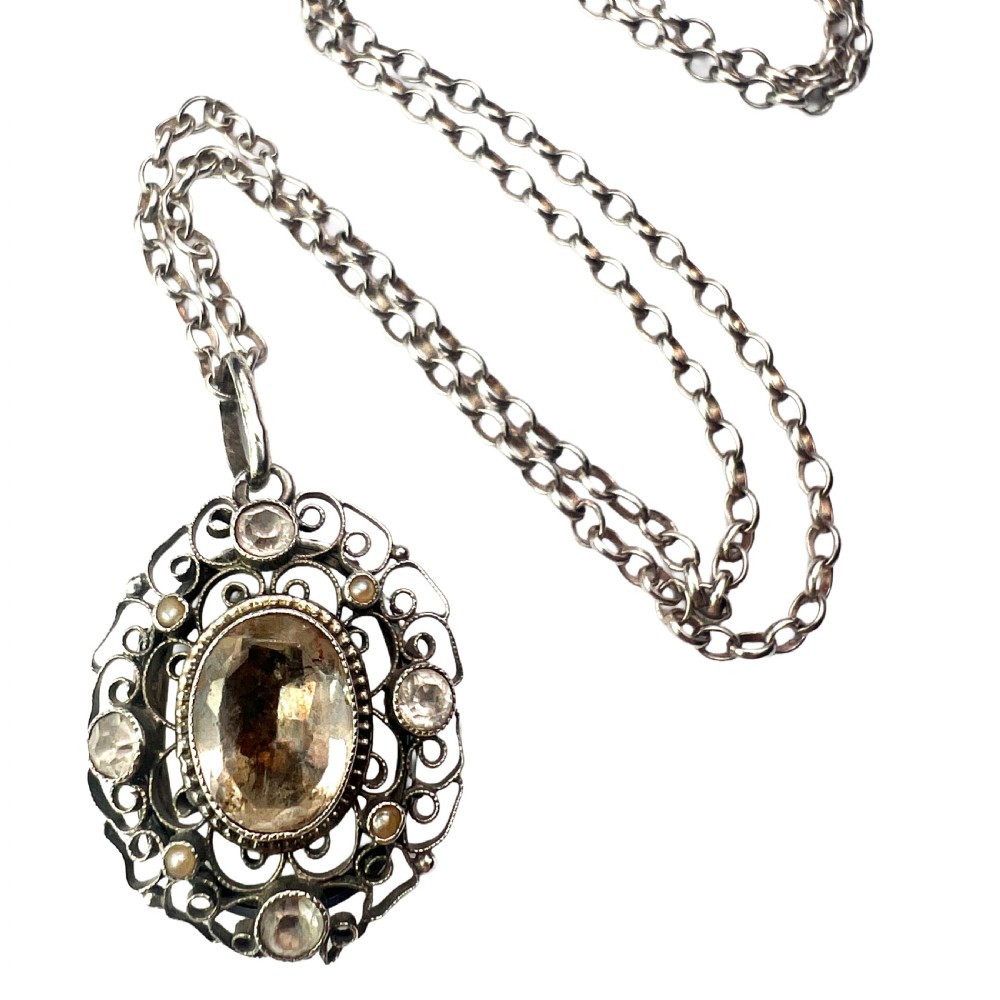 An antique silver filigree oval locket pendant featuring a central oval faceted stone surrounded by delicate wirework scrollwork and seed pearl accents on a silver chain.