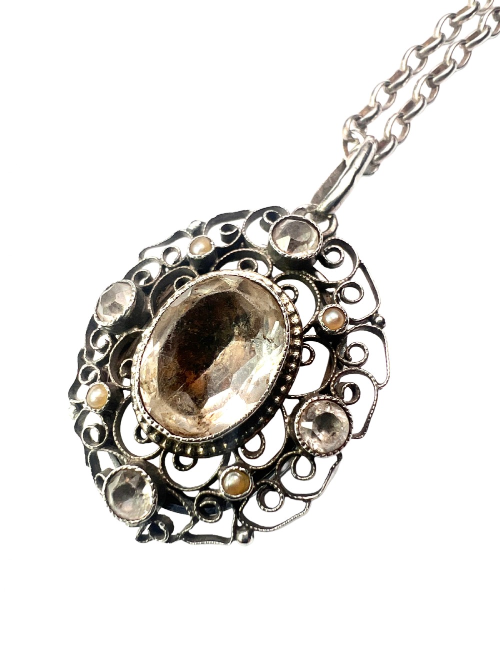 An antique silver filigree oval locket pendant featuring a central oval faceted stone surrounded by delicate wirework scrollwork and seed pearl accents on a silver chain. View IV