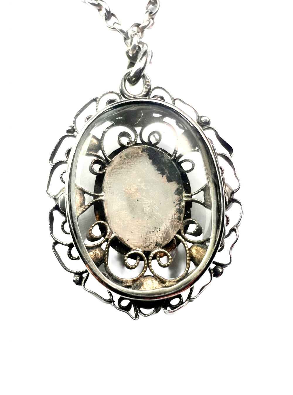 An antique silver filigree oval locket pendant featuring a central oval faceted stone surrounded by delicate wirework scrollwork and seed pearl accents on a silver chain. View V