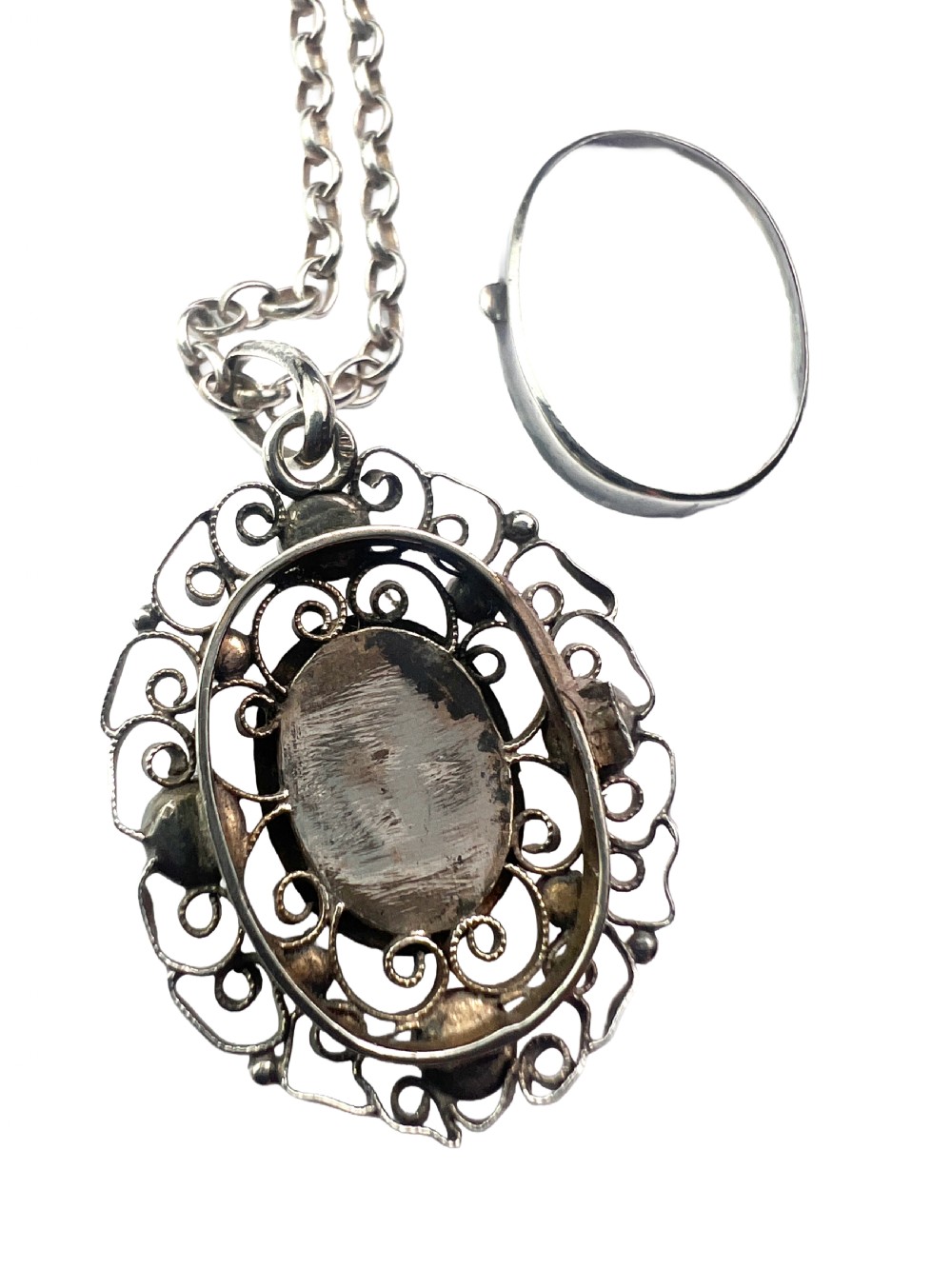 An antique silver filigree oval locket pendant featuring a central oval faceted stone surrounded by delicate wirework scrollwork and seed pearl accents on a silver chain. View VII