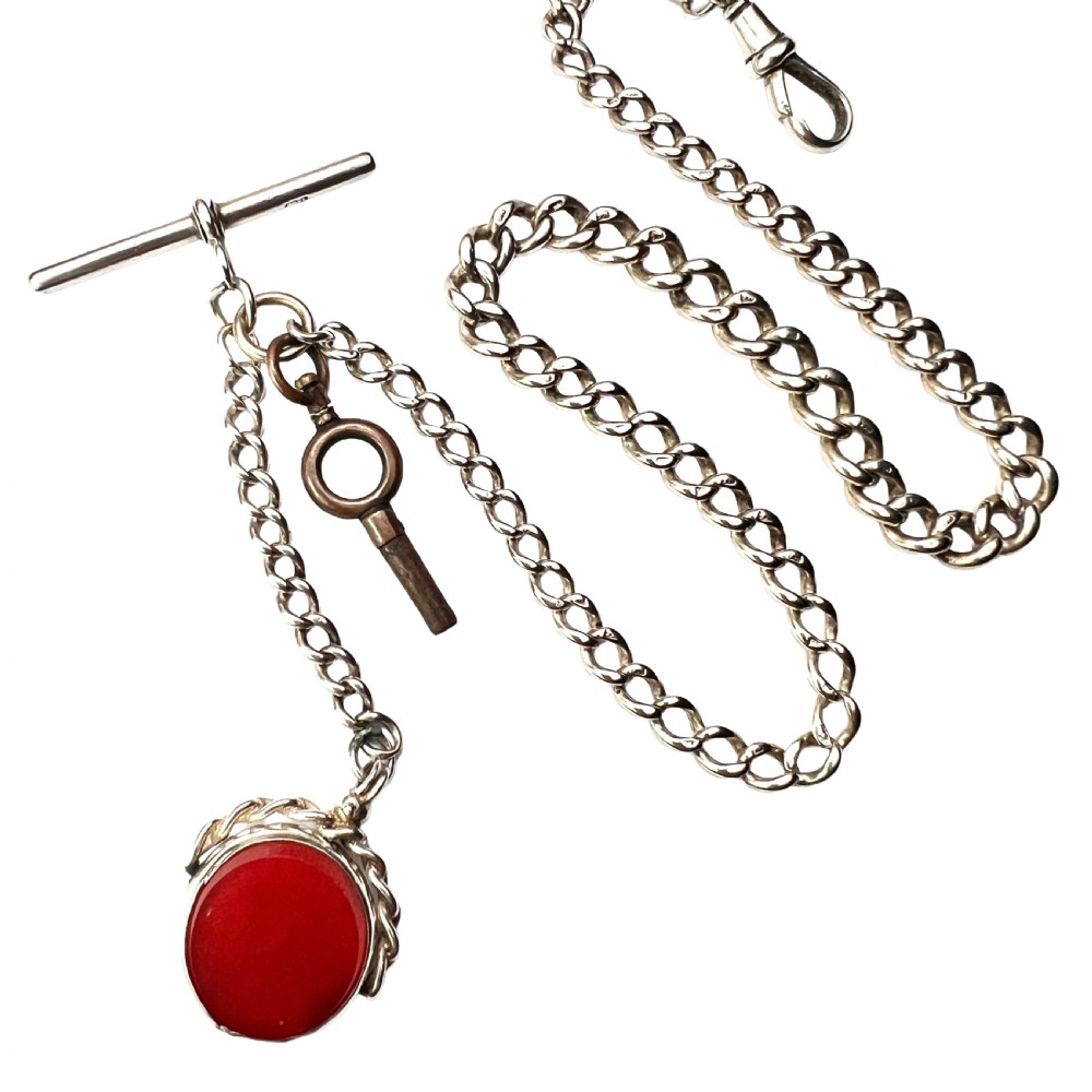 A Victorian sterling silver curb link Albert watch chain featuring a T-bar, watch key charm, and red stone swivel fob.