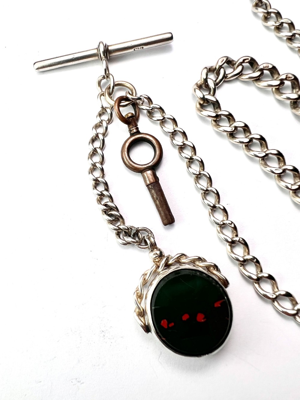 A Victorian sterling silver curb link Albert watch chain featuring a T-bar, watch key charm, and red stone swivel fob. View III