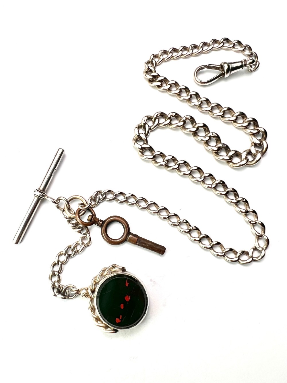 A Victorian sterling silver curb link Albert watch chain featuring a T-bar, watch key charm, and red stone swivel fob. View IV