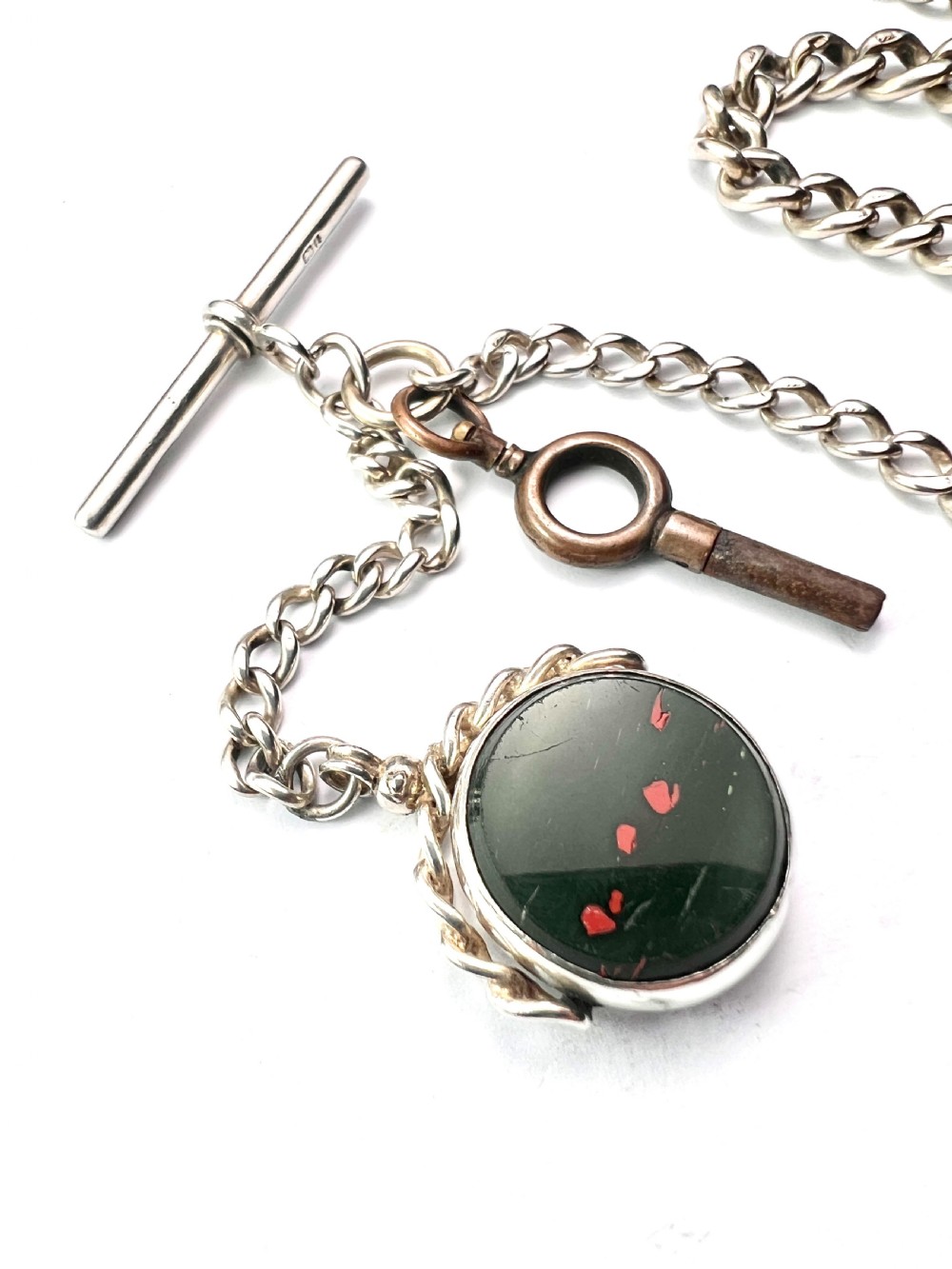 A Victorian sterling silver curb link Albert watch chain featuring a T-bar, watch key charm, and red stone swivel fob. View V