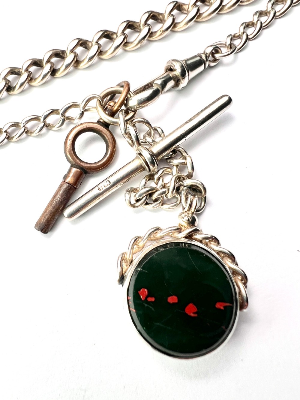 A Victorian sterling silver curb link Albert watch chain featuring a T-bar, watch key charm, and red stone swivel fob. View VII