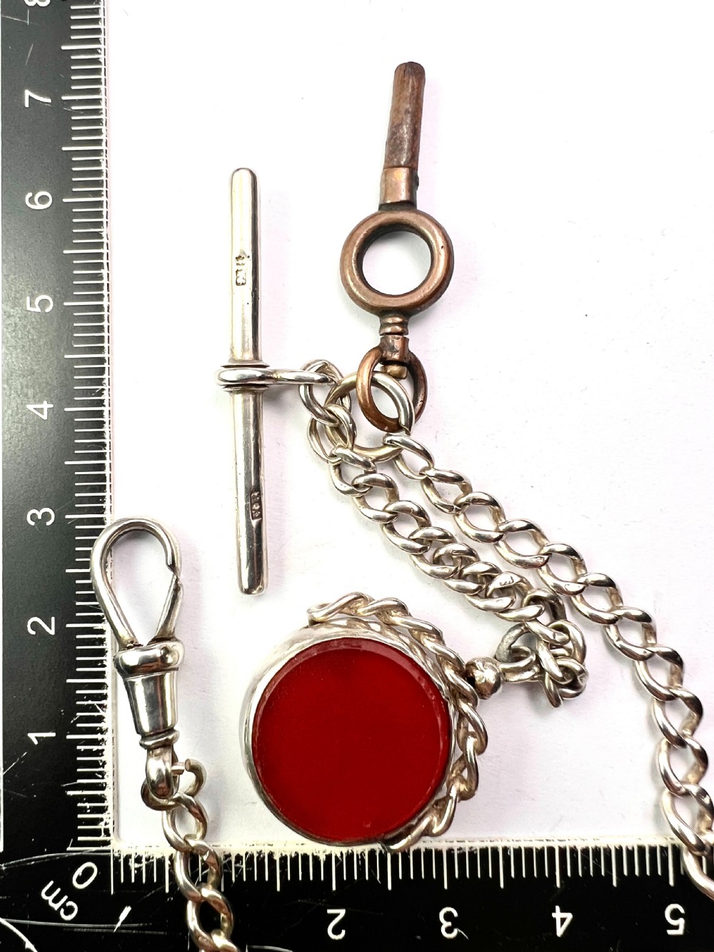 A Victorian sterling silver curb link Albert watch chain featuring a T-bar, watch key charm, and red stone swivel fob. View VIII