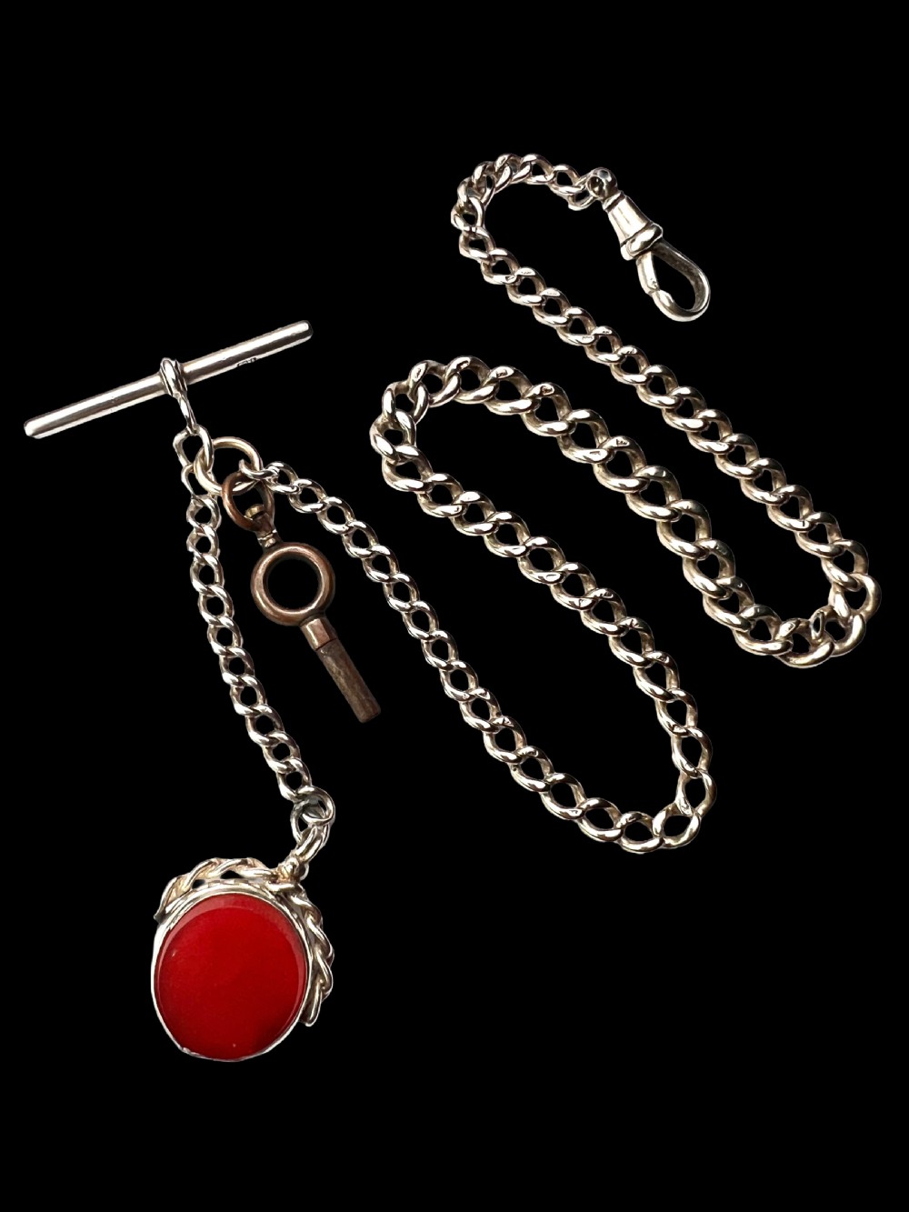 A Victorian sterling silver curb link Albert watch chain featuring a T-bar, watch key charm, and red stone swivel fob. View IX