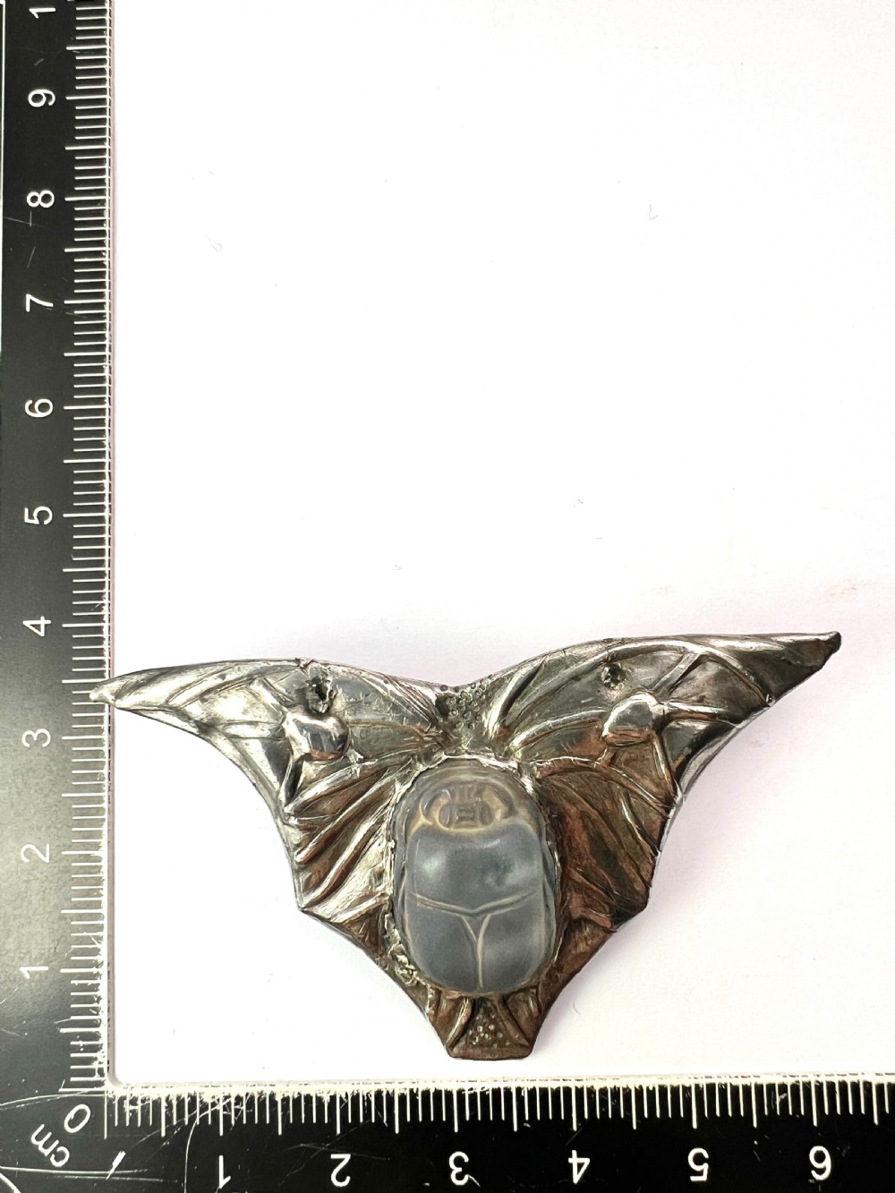 An antique pewter Art Nouveau brooch featuring a central translucent scarab beetle cabochon flanked by outstretched stylized wings. View IX
