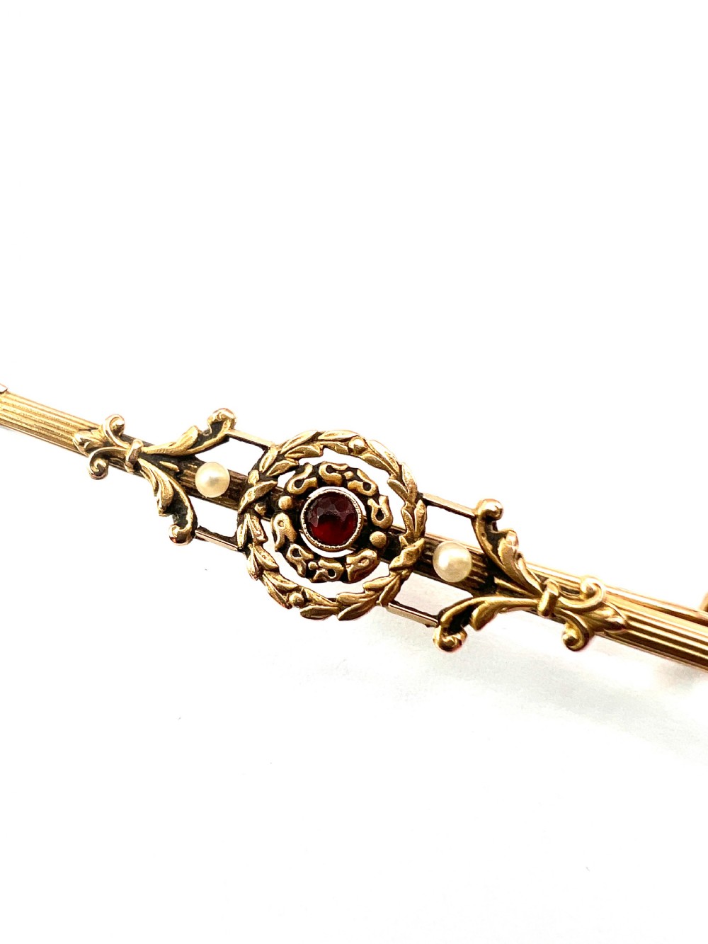 An antique 18-carat yellow gold bar brooch featuring a central circular motif with a round red garnet flanked by seed pearls and fluted bar details. View II