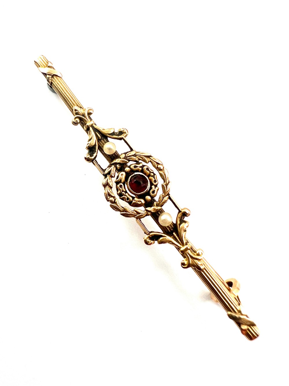 An antique 18-carat yellow gold bar brooch featuring a central circular motif with a round red garnet flanked by seed pearls and fluted bar details. View III