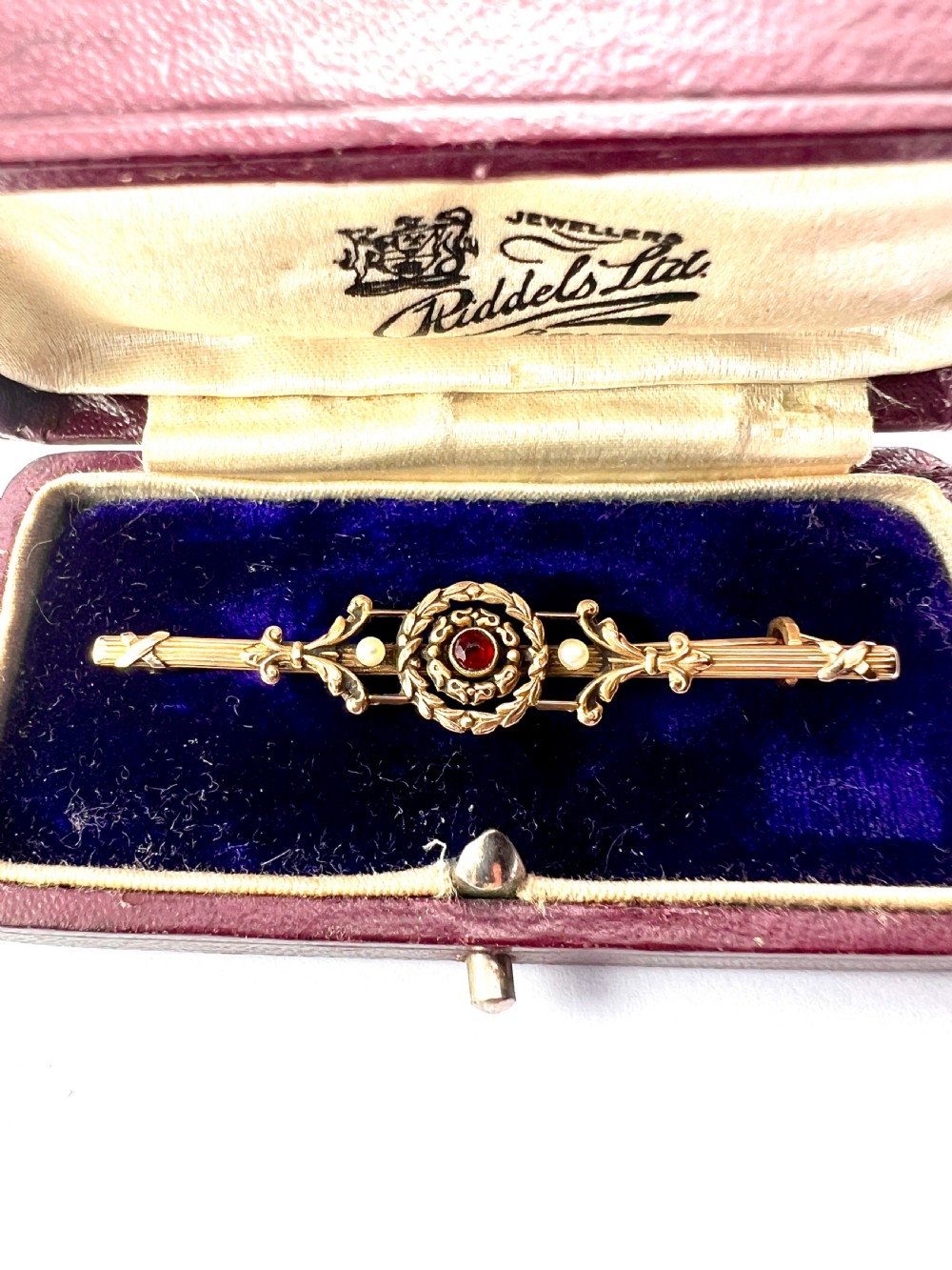 An antique 18-carat yellow gold bar brooch featuring a central circular motif with a round red garnet flanked by seed pearls and fluted bar details. View IV