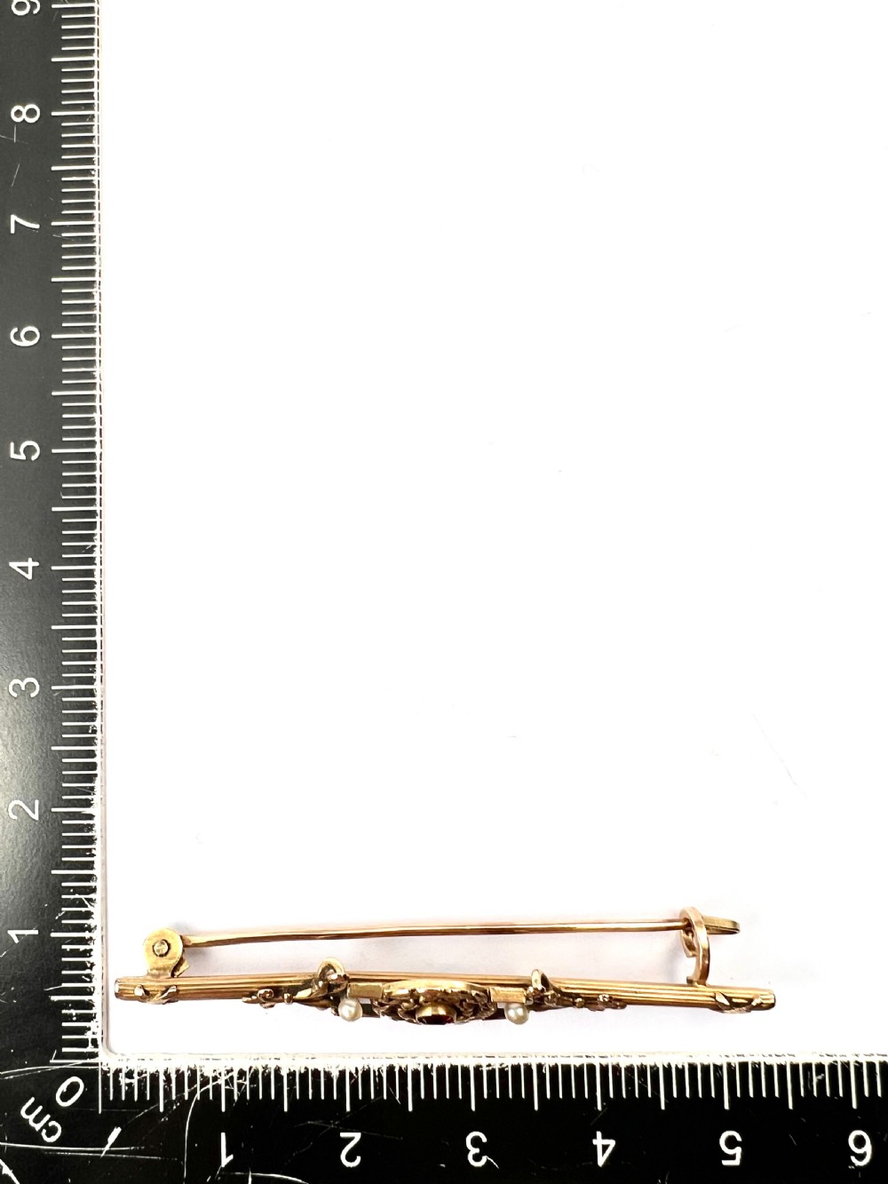 An antique 18-carat yellow gold bar brooch featuring a central circular motif with a round red garnet flanked by seed pearls and fluted bar details. View IX