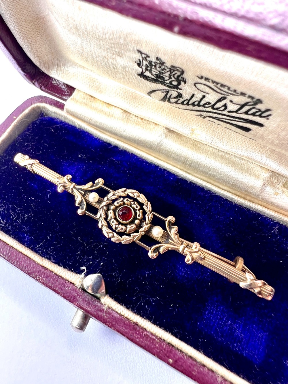 An antique 18-carat yellow gold bar brooch featuring a central circular motif with a round red garnet flanked by seed pearls and fluted bar details. View X
