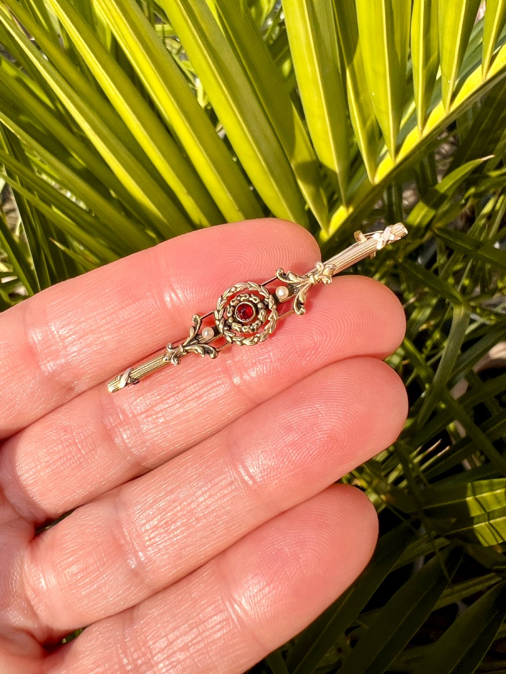 An antique 18-carat yellow gold bar brooch featuring a central circular motif with a round red garnet flanked by seed pearls and fluted bar details. View XI