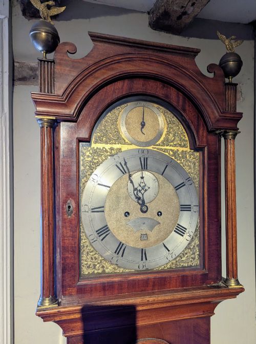 fig 1. An 18th-century Georgian flame mahogany longcase clock featuring an arched hood with brass eagle finials and an engraved brass dial.