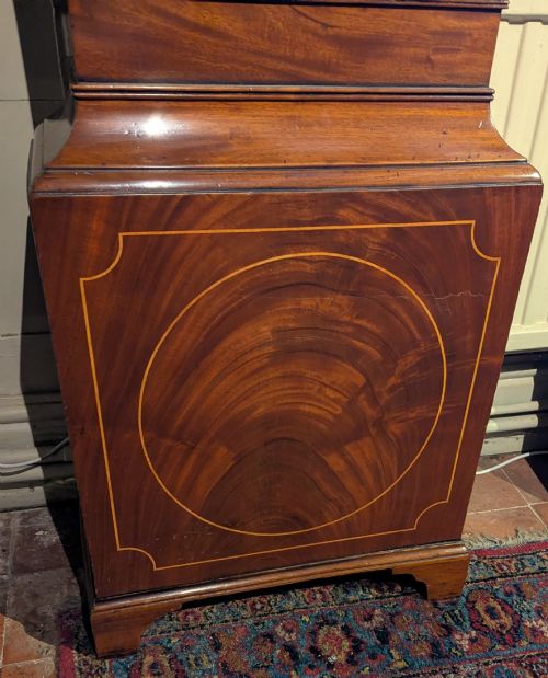 fig 1. An early nineteenth-century flame mahogany longcase clock featuring a swan-neck pediment, brass dial with a painted moon phase arch, and oval stringing on the trunk door.