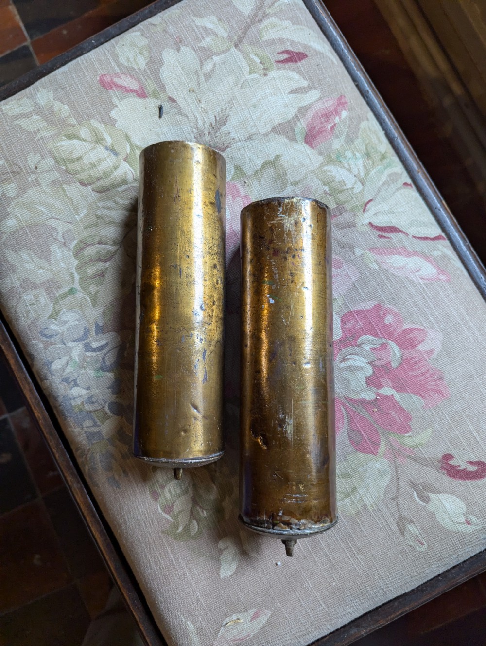 A pair of cylindrical eighteenth-century brass-cased longcase clock weights showing surface oxidation and original metal wear.