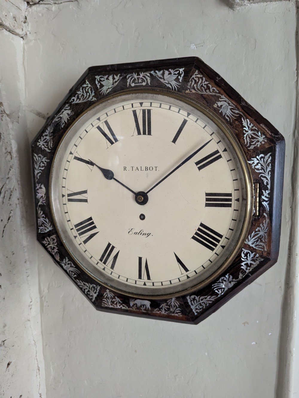 An octagonal 19th-century rosewood wall clock with intricate mother-of-pearl floral inlay and a white painted dial with Roman numerals.