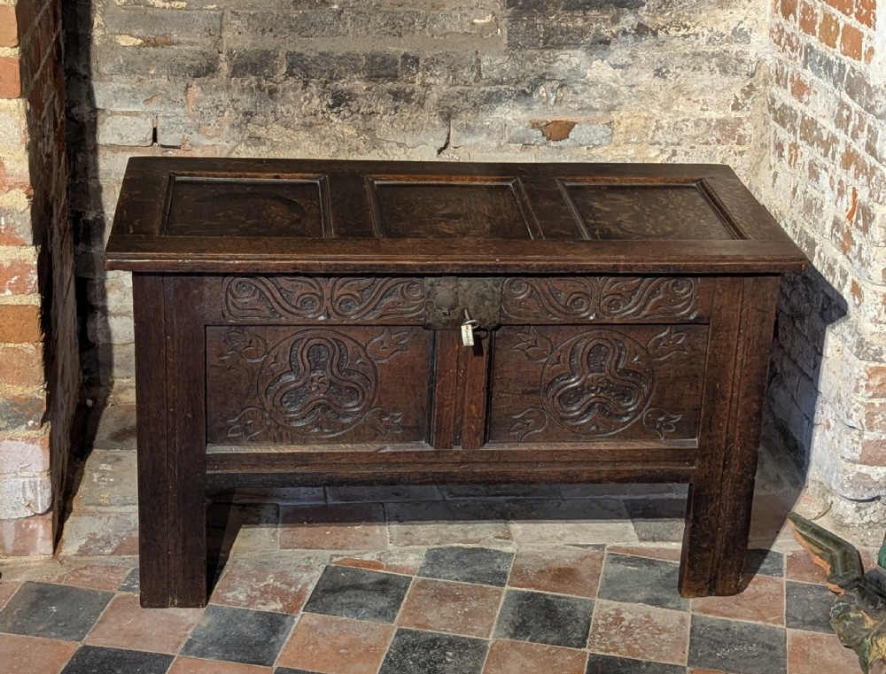 A small 17th-century dark oak coffer featuring carved foliate front panels, a three-panel hinged lid, and an iron lock plate.