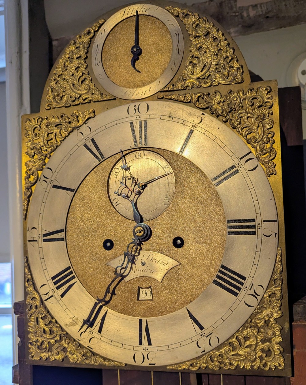 An 18th-century mahogany longcase clock featuring brass eagle finials, an arched dial hood, and a flame mahogany trunk door. View VI