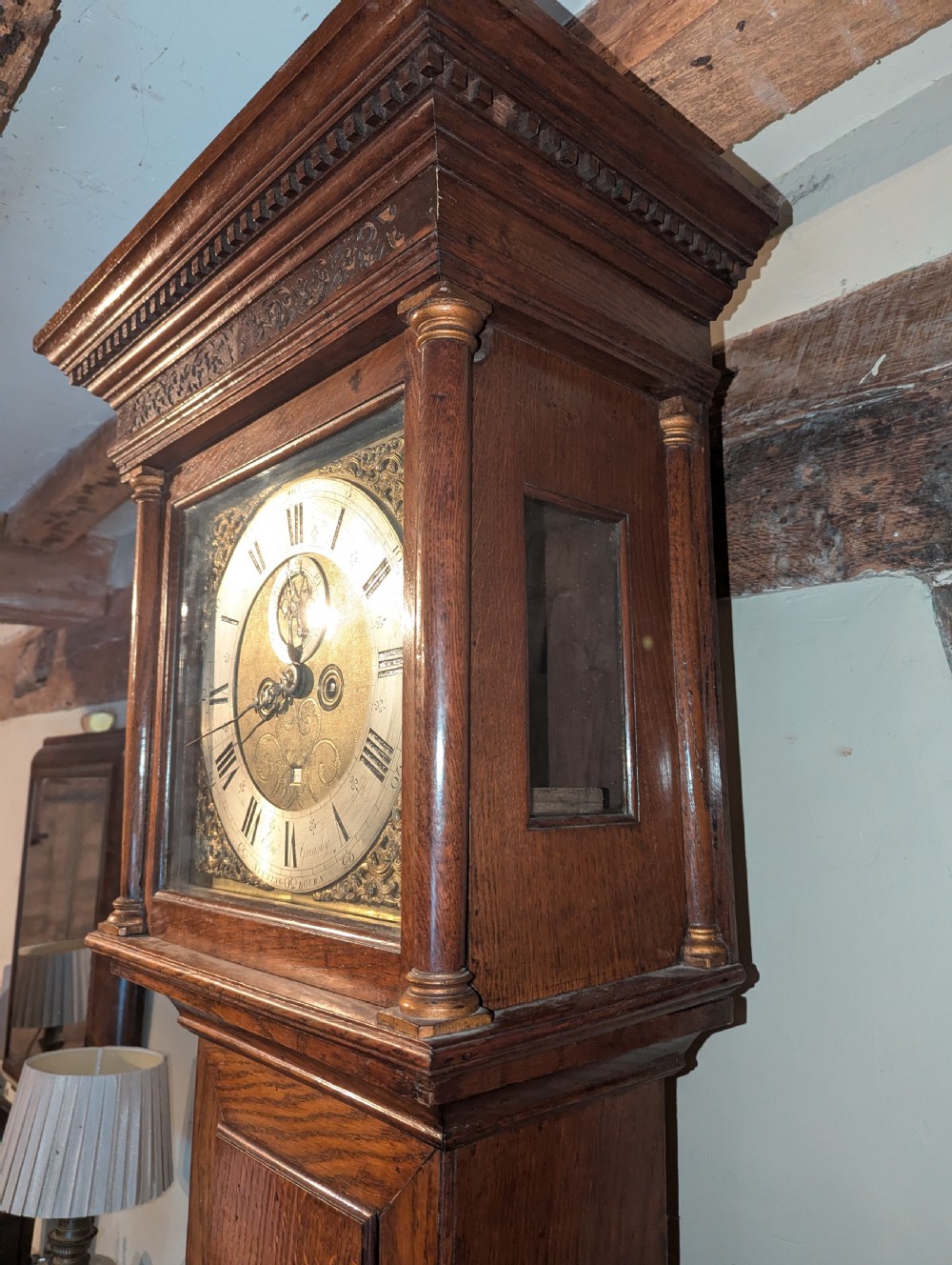 An 18th-century oak longcase clock featuring a square brass dial with spandrels, a moulded hood, and a slender wooden trunk. View IV