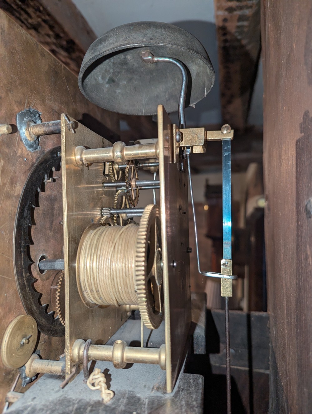 An 18th-century oak longcase clock featuring a square brass dial with spandrels, a moulded hood, and a slender wooden trunk. View V