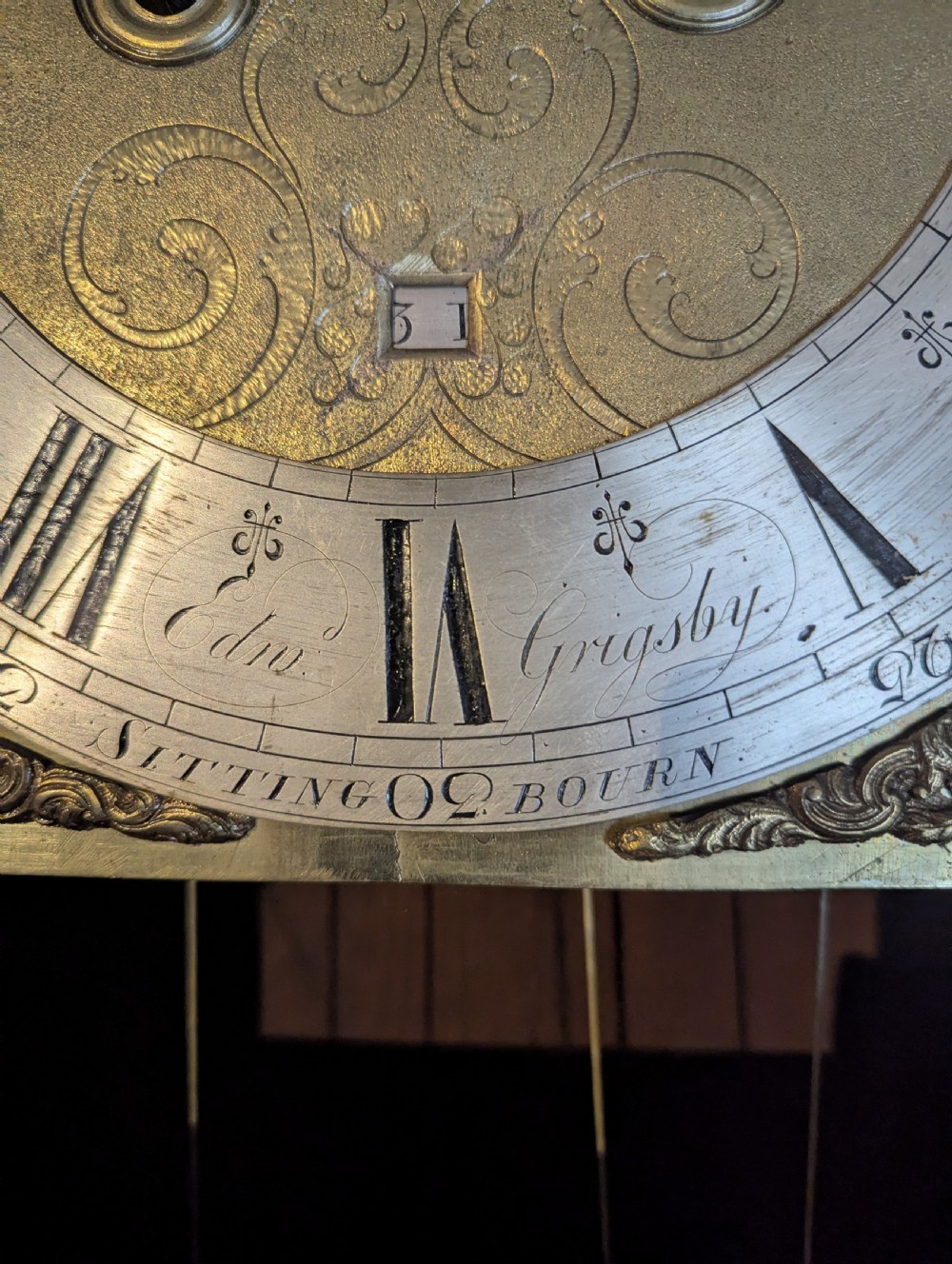 An 18th-century oak longcase clock featuring a square brass dial with spandrels, a moulded hood, and a slender wooden trunk. View VI