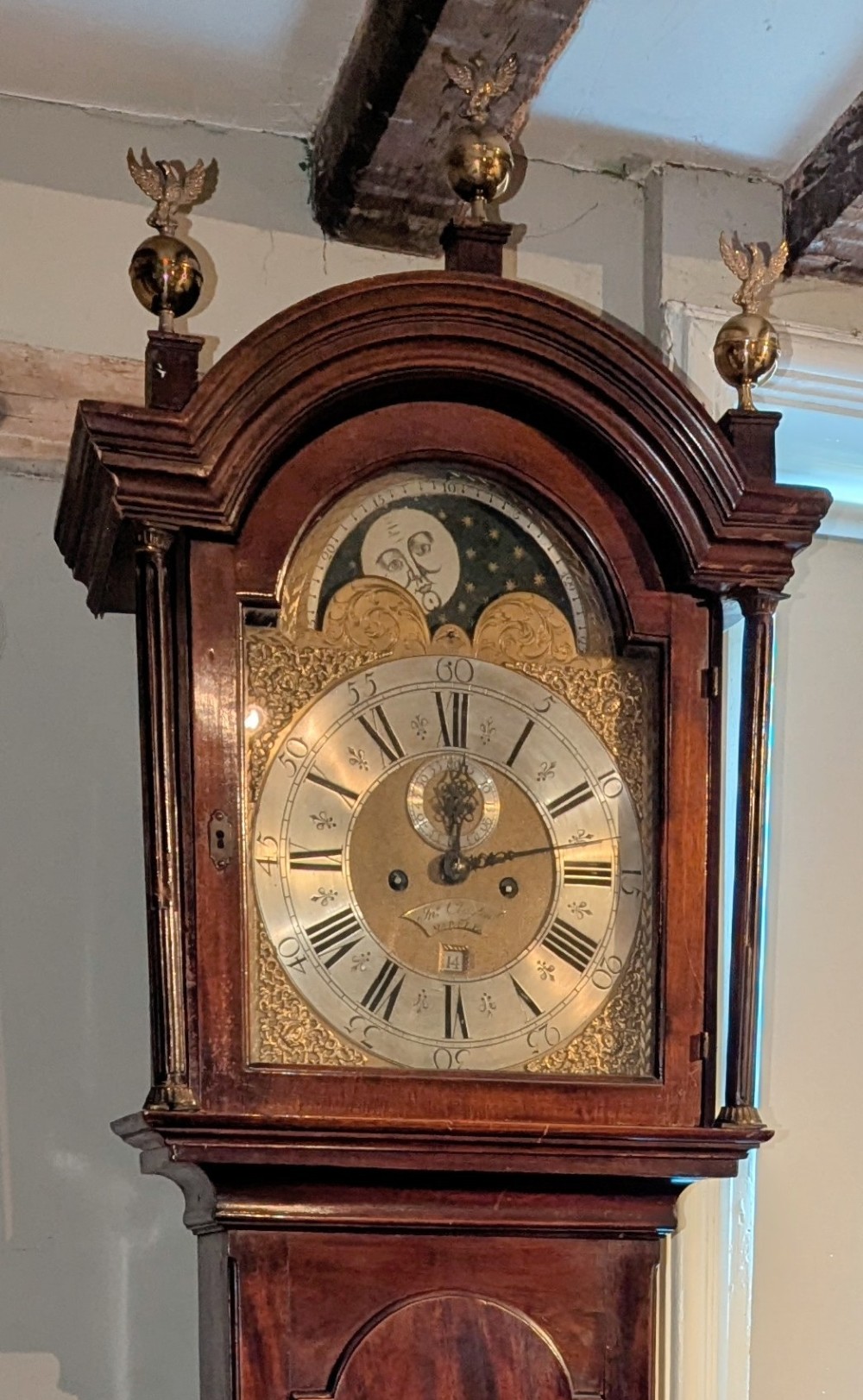 An eighteenth-century Georgian mahogany longcase clock with an arched hood, three brass eagle finials, and an engraved brass moon phase dial. View II