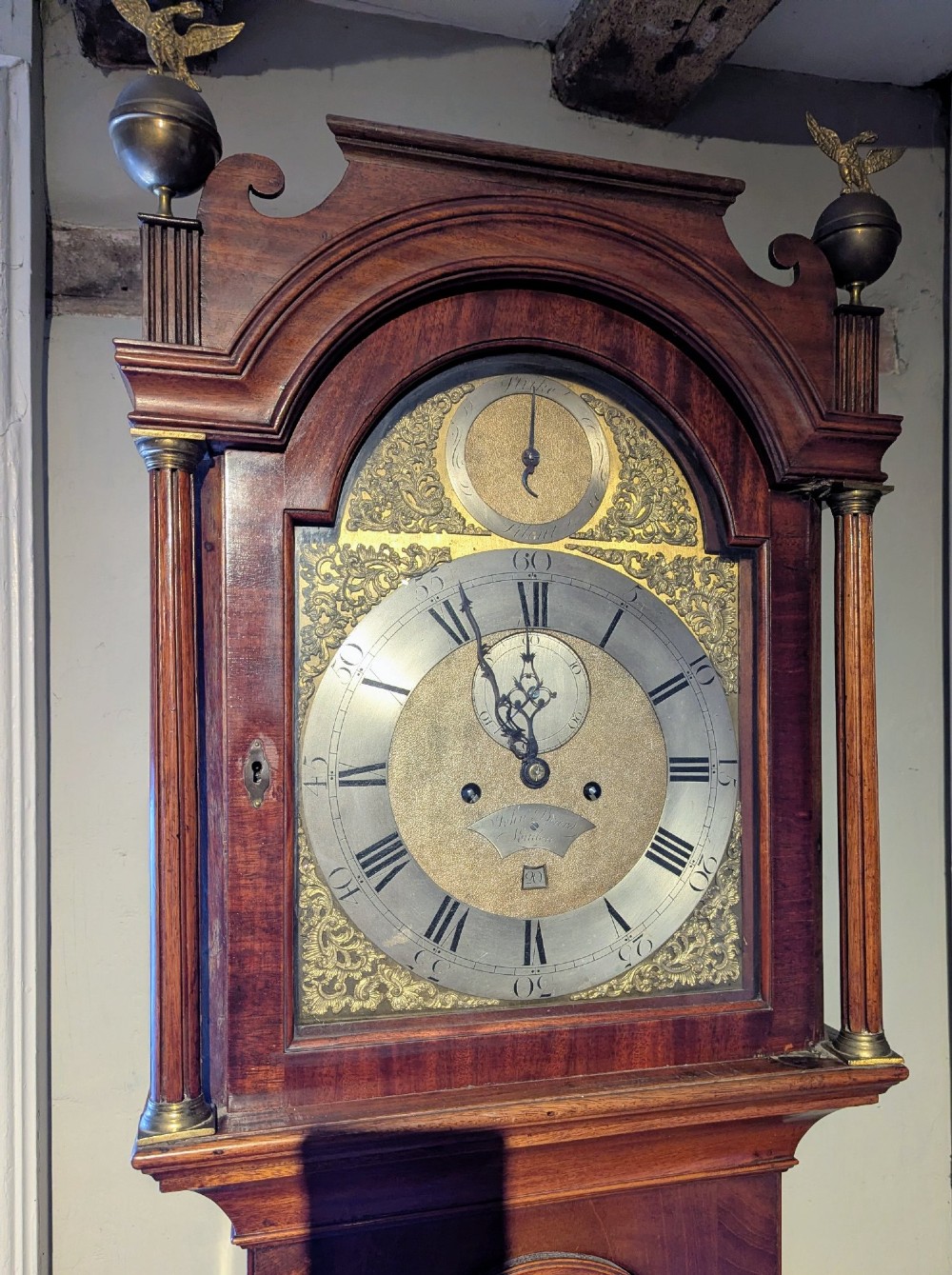 An 18th-century Georgian flame mahogany longcase clock featuring an arched hood with brass eagle finials and an engraved brass dial. View II