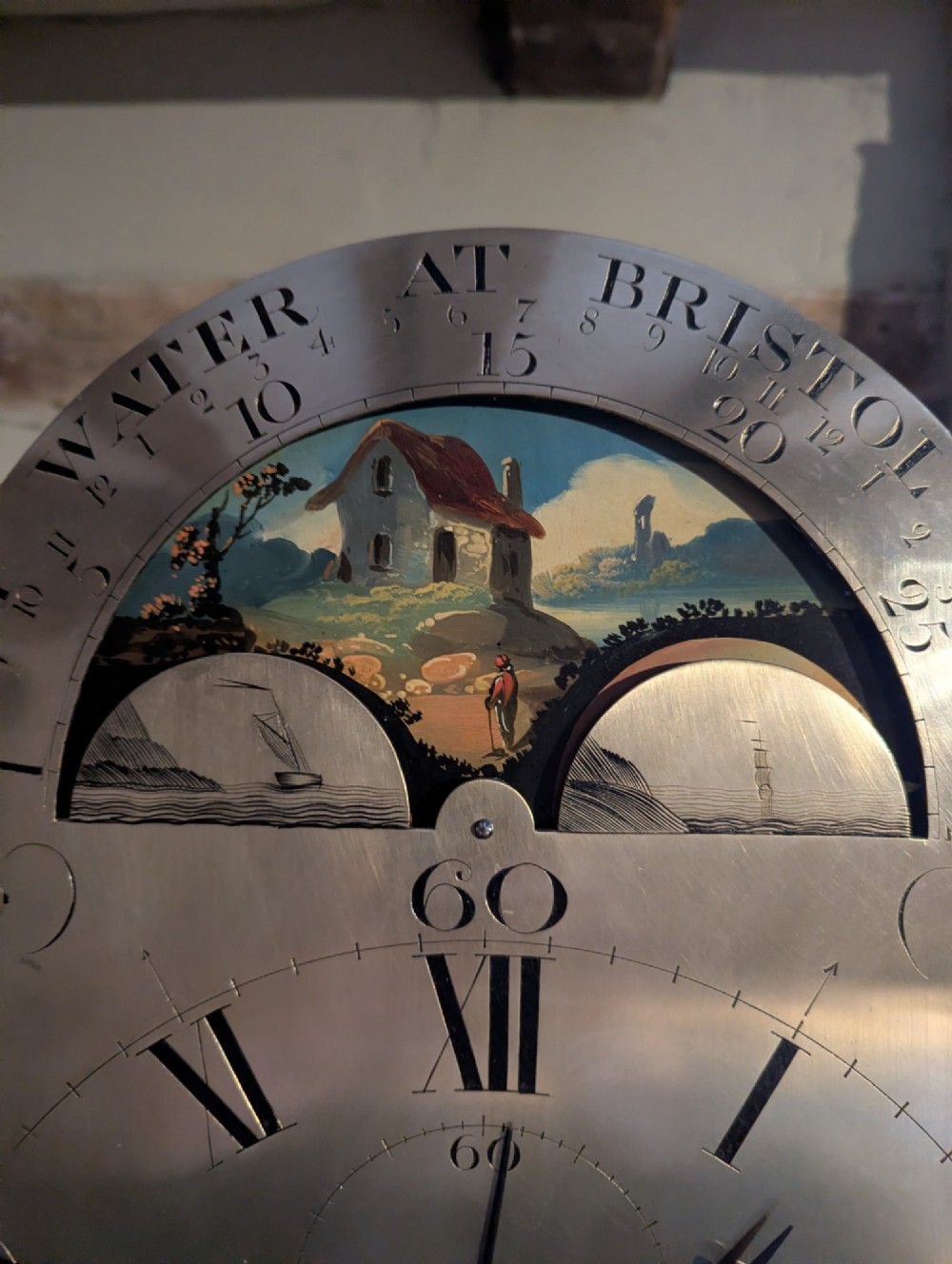 An early nineteenth-century flame mahogany longcase clock featuring a swan-neck pediment, brass dial with a painted moon phase arch, and oval stringing on the trunk door. View VI