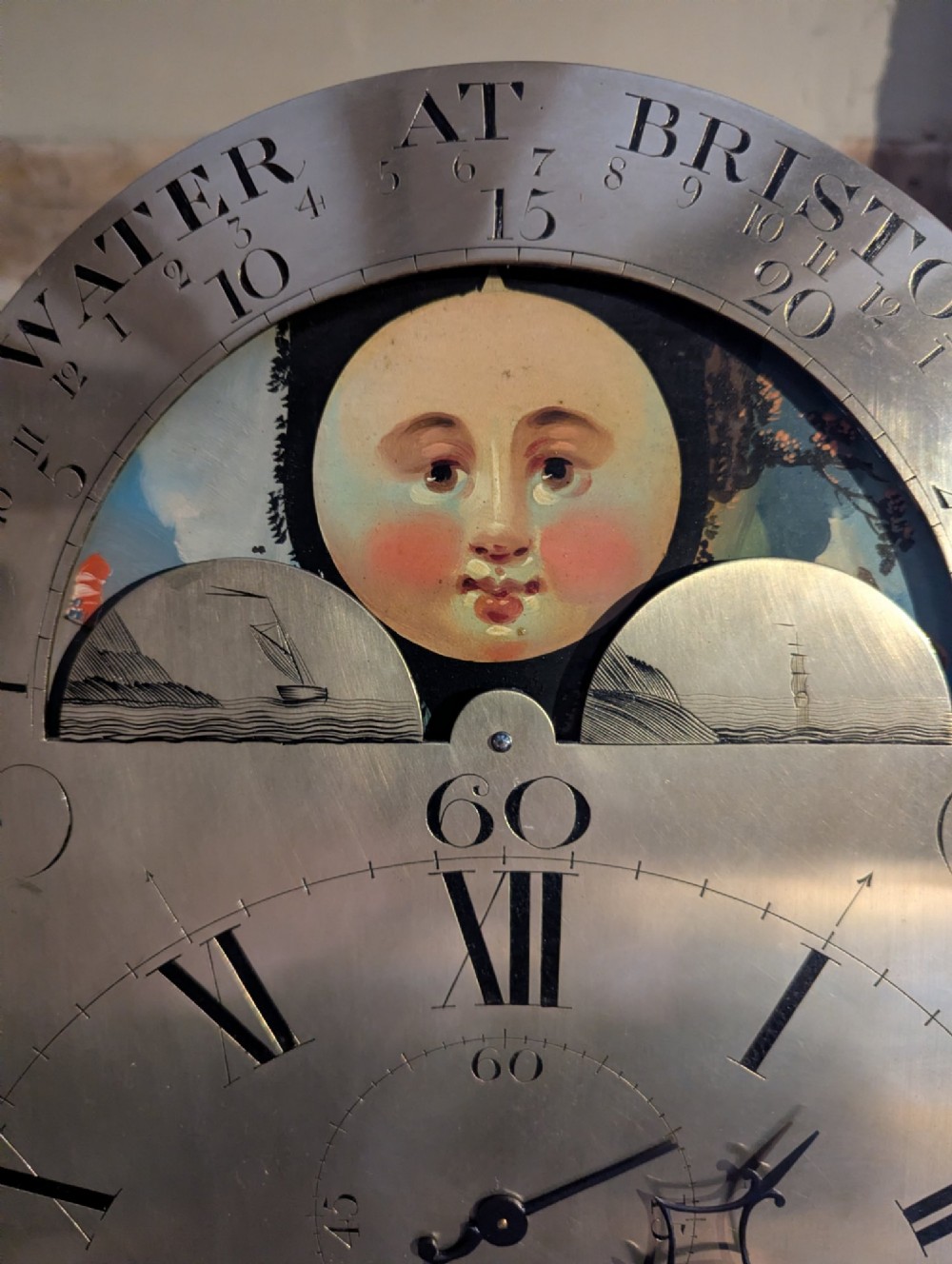 An early nineteenth-century flame mahogany longcase clock featuring a swan-neck pediment, brass dial with a painted moon phase arch, and oval stringing on the trunk door. View VII