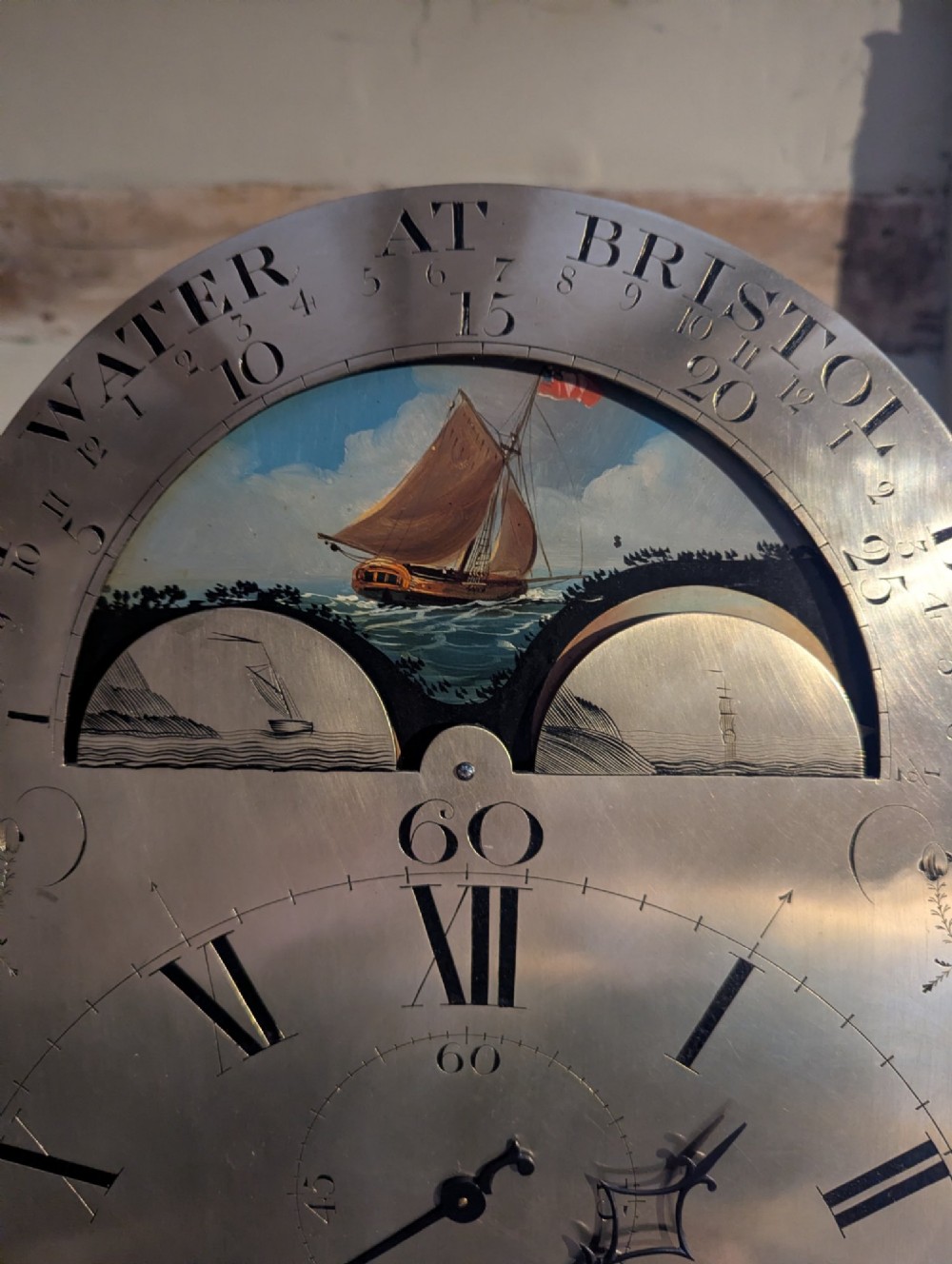 An early nineteenth-century flame mahogany longcase clock featuring a swan-neck pediment, brass dial with a painted moon phase arch, and oval stringing on the trunk door. View VIII