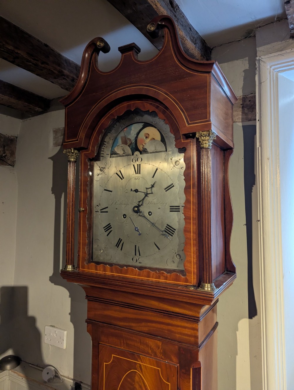 An early nineteenth-century flame mahogany longcase clock featuring a swan-neck pediment, brass dial with a painted moon phase arch, and oval stringing on the trunk door. View IX