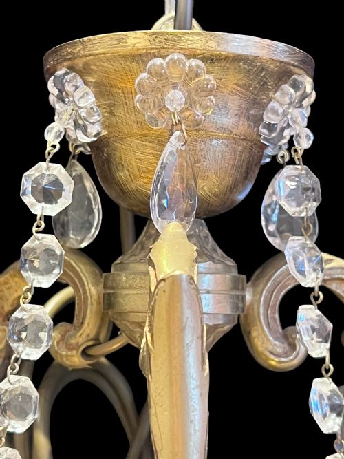 fig 1. A French brass six-light chandelier decorated with faceted crystal drops, bead swags, scrolled metal arms, and cream candle-effect sleeves.