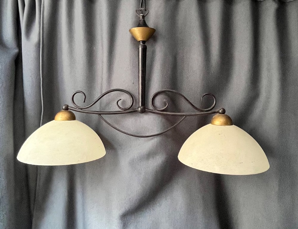 A 1940s French two-light downlighter featuring a black wrought-iron frame with scrollwork, brass accents, and two cream frosted glass dome shades.