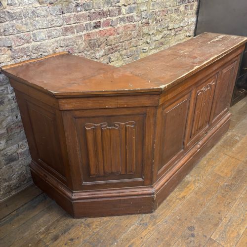 fig 1. An angled Edwardian oak commercial shop counter featuring recessed timber panels with carved decorative motifs and a heavy plinth base.