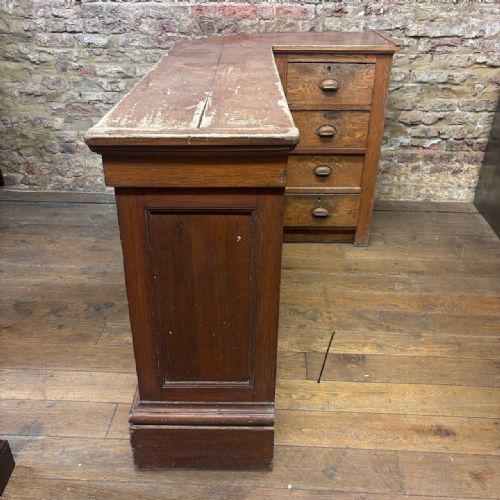 fig 2. An angled Edwardian oak commercial shop counter featuring recessed timber panels with carved decorative motifs and a heavy plinth base.