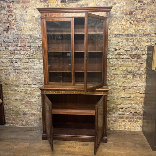 fig 1. An early 20th-century dark oak school library bookcase with glazed upper doors, lower panel doors featuring carved institutional text, and adjustable interior shelving.