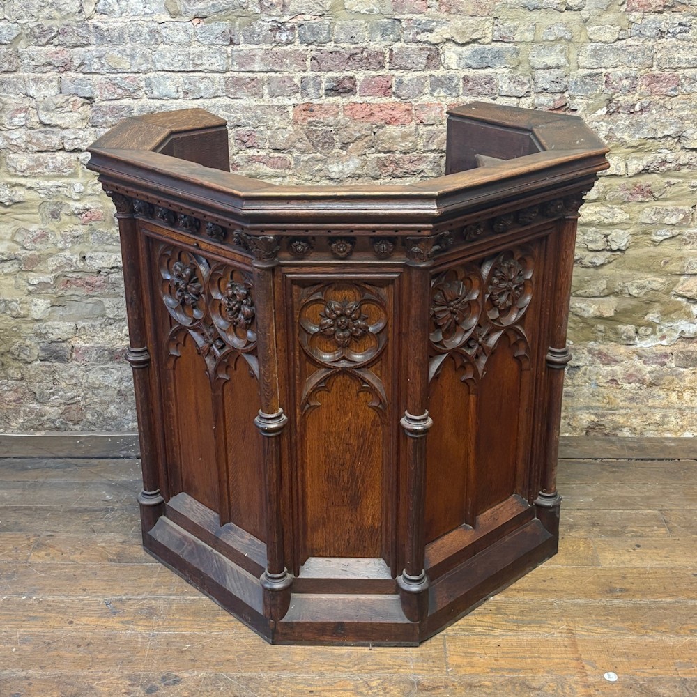A late nineteenth-century carved oak church pulpit featuring Gothic tracery, floral medallions, and integrated corner columns.