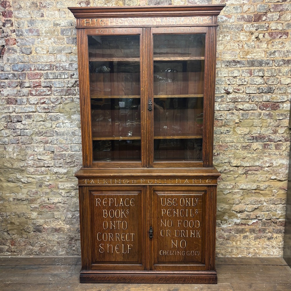 An early 20th-century dark oak school library bookcase with glazed upper doors, lower panel doors featuring carved institutional text, and adjustable interior shelving.
