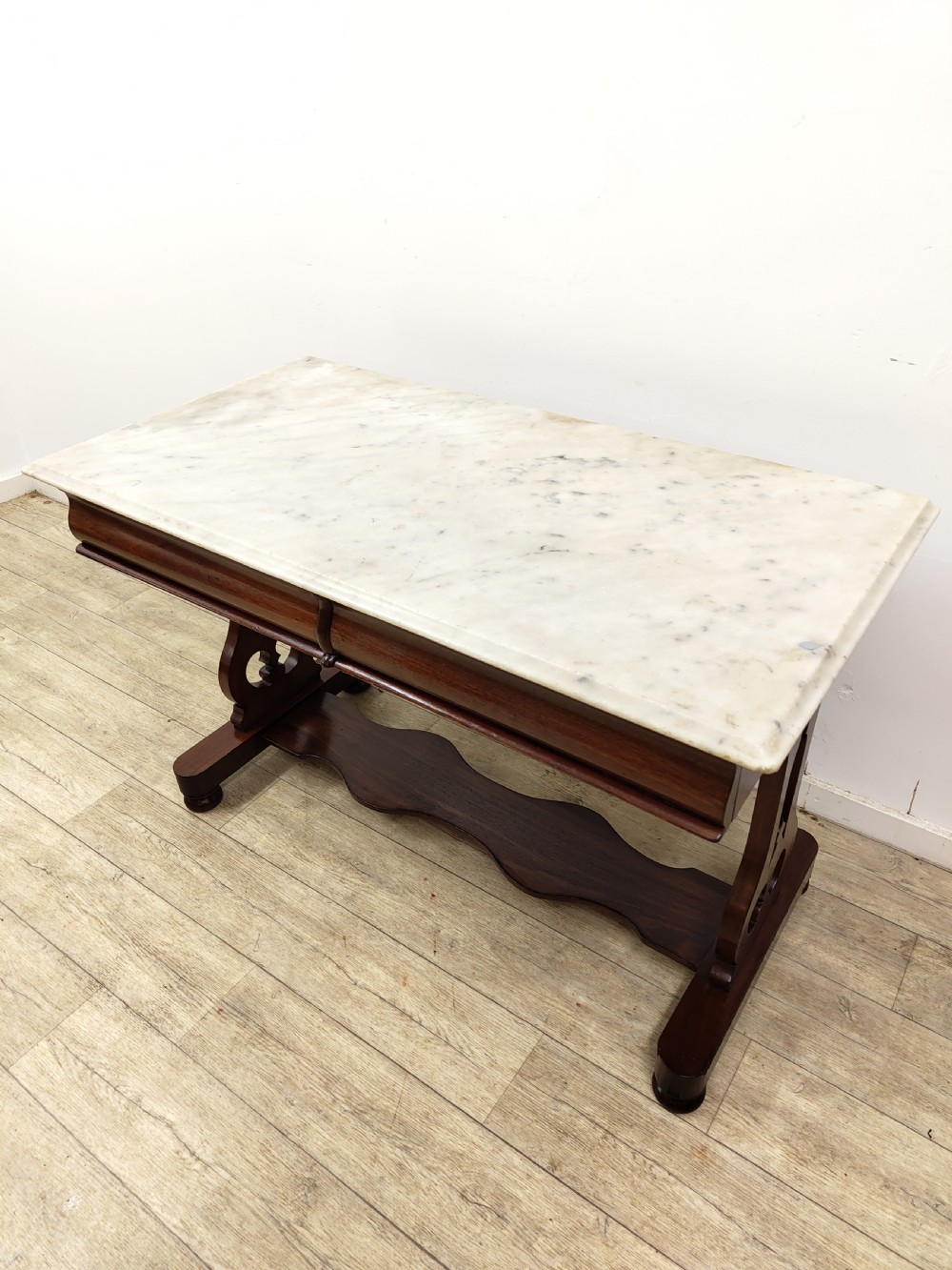 A Victorian mahogany washstand with a rectangular white marble top resting on twin pierced trestle supports linked by a shaped stretcher. View IV