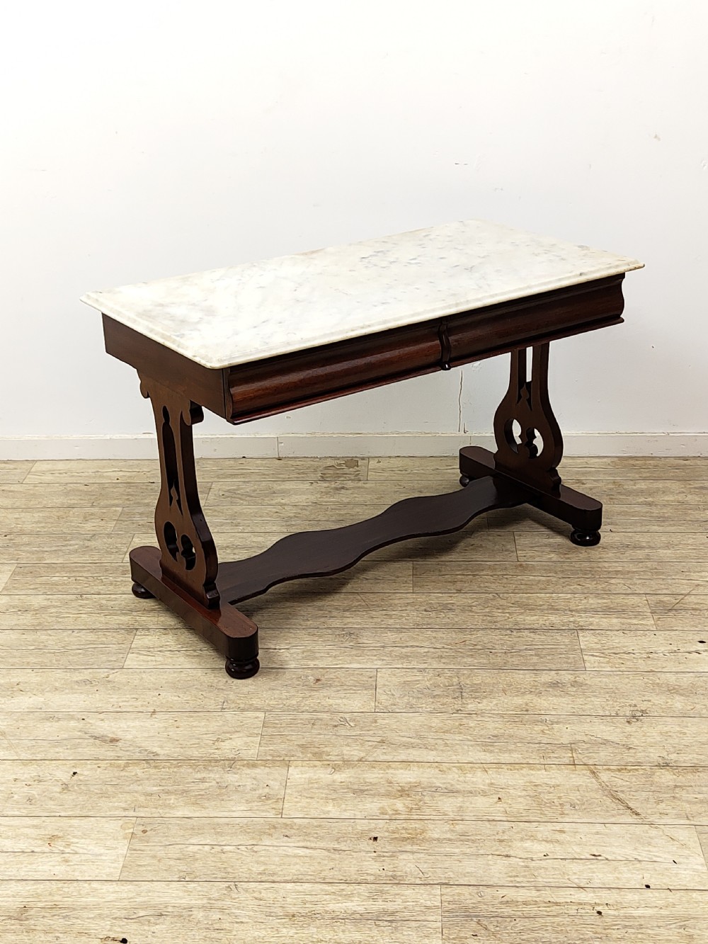 A Victorian mahogany washstand with a rectangular white marble top resting on twin pierced trestle supports linked by a shaped stretcher.