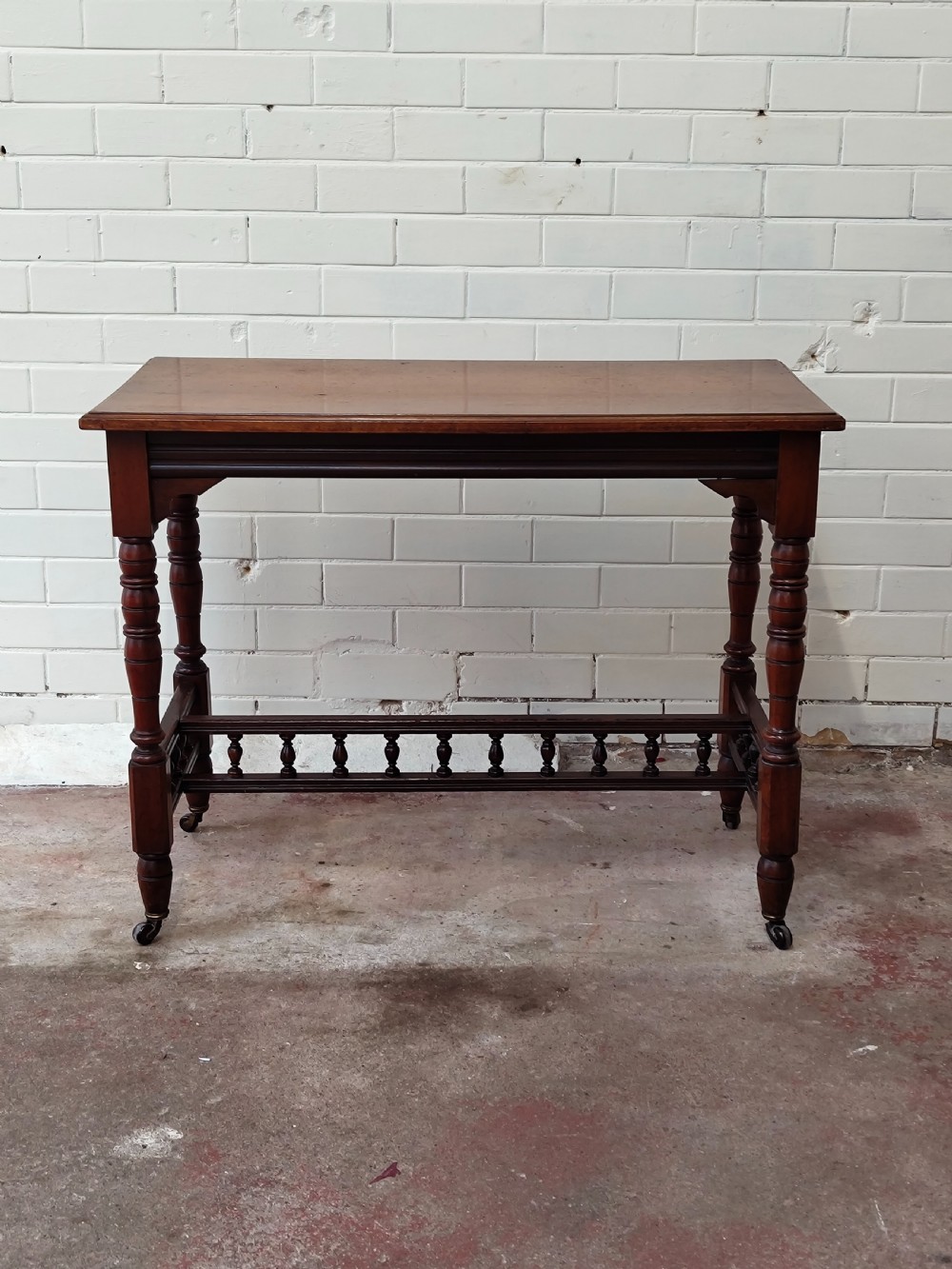 A solid walnut rectangular centre table featuring turned legs, a spindle-galleried lower stretcher, and brass castors. View IV