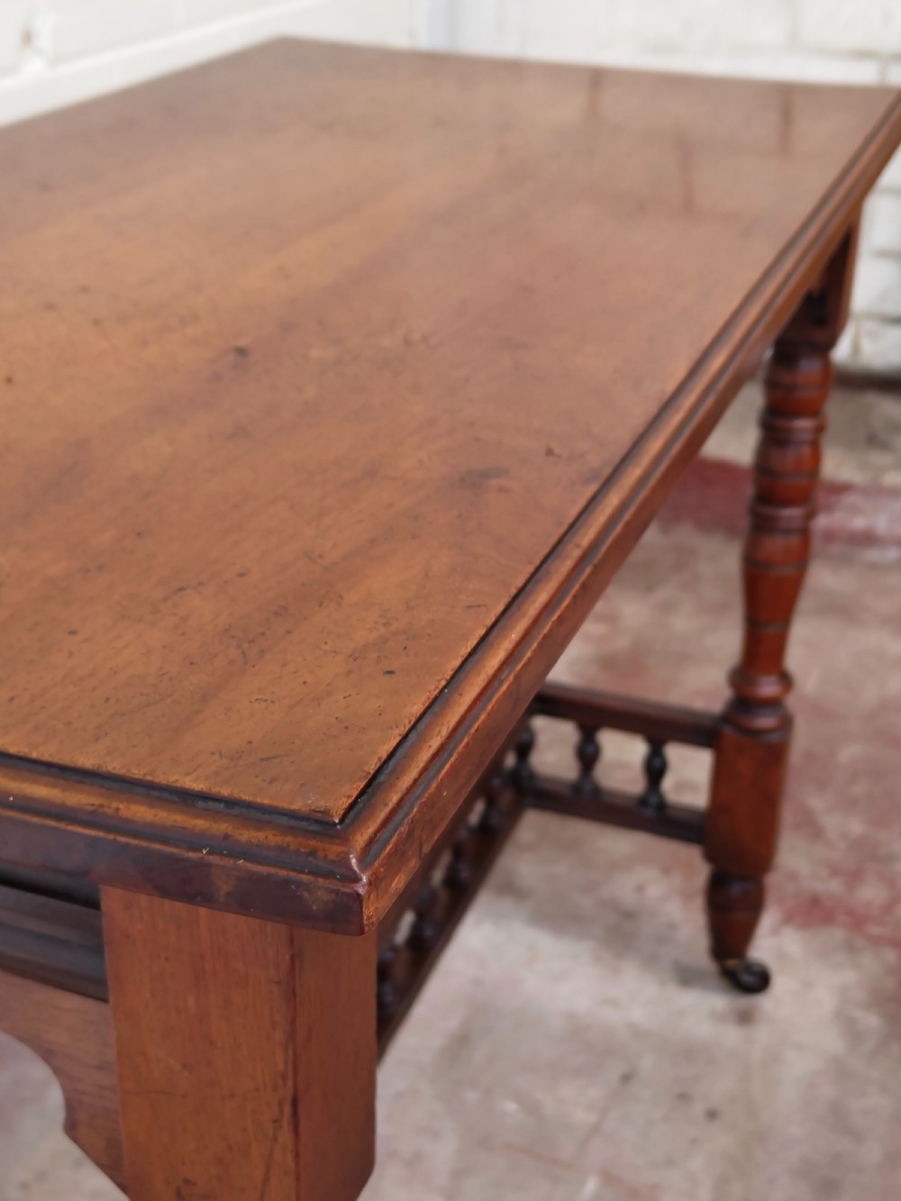 A solid walnut rectangular centre table featuring turned legs, a spindle-galleried lower stretcher, and brass castors. View VI