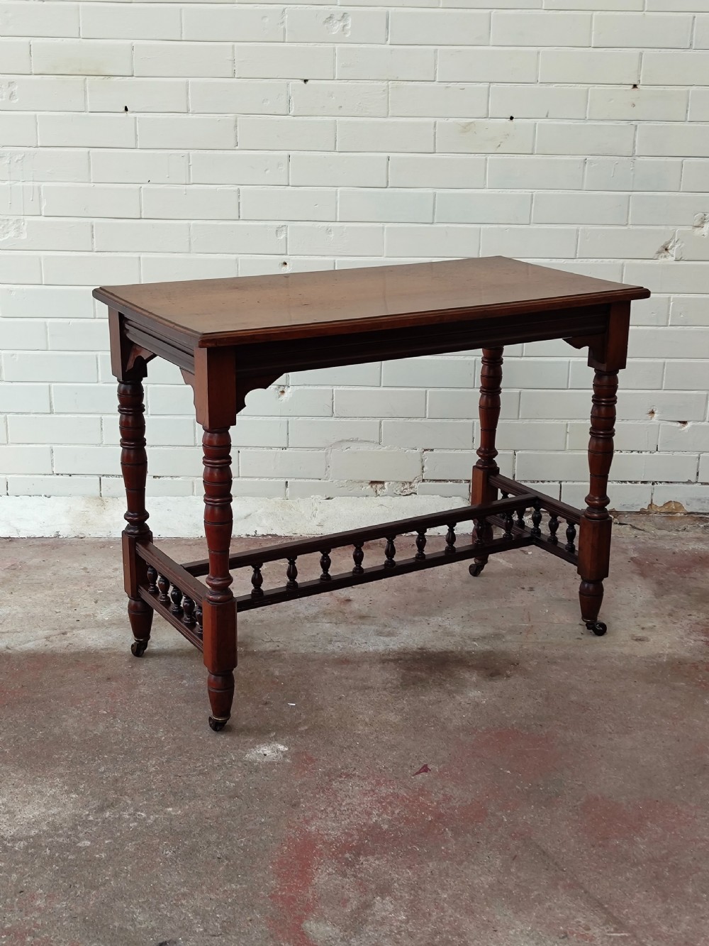 A solid walnut rectangular centre table featuring turned legs, a spindle-galleried lower stretcher, and brass castors. View VII