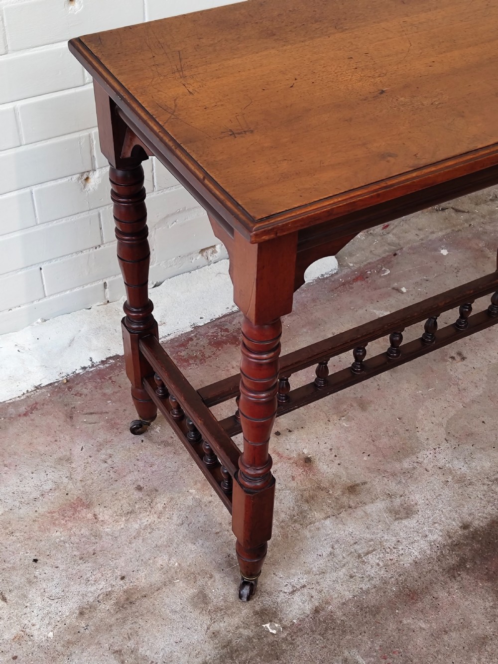 A solid walnut rectangular centre table featuring turned legs, a spindle-galleried lower stretcher, and brass castors. View X