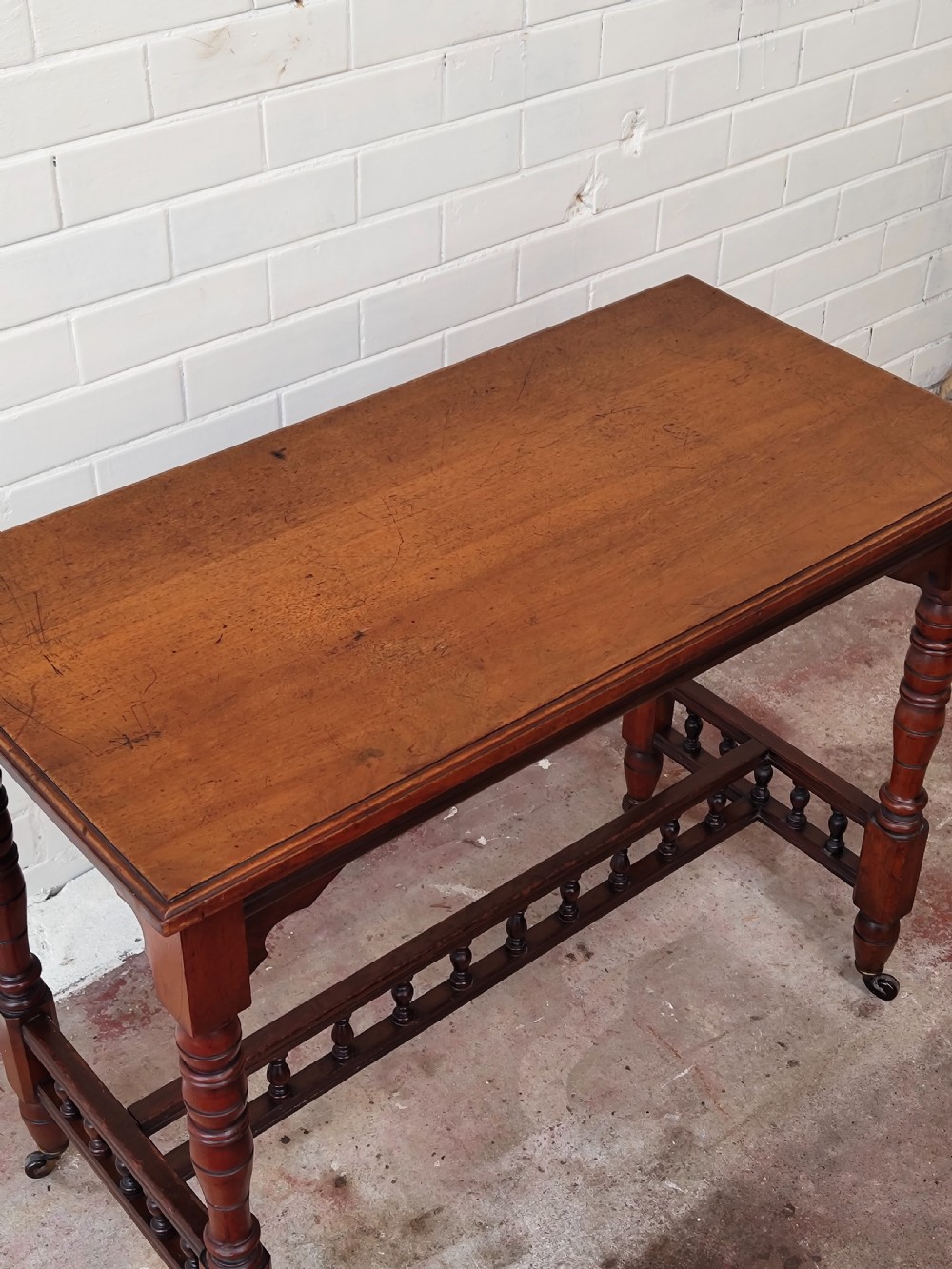 A solid walnut rectangular centre table featuring turned legs, a spindle-galleried lower stretcher, and brass castors. View XI